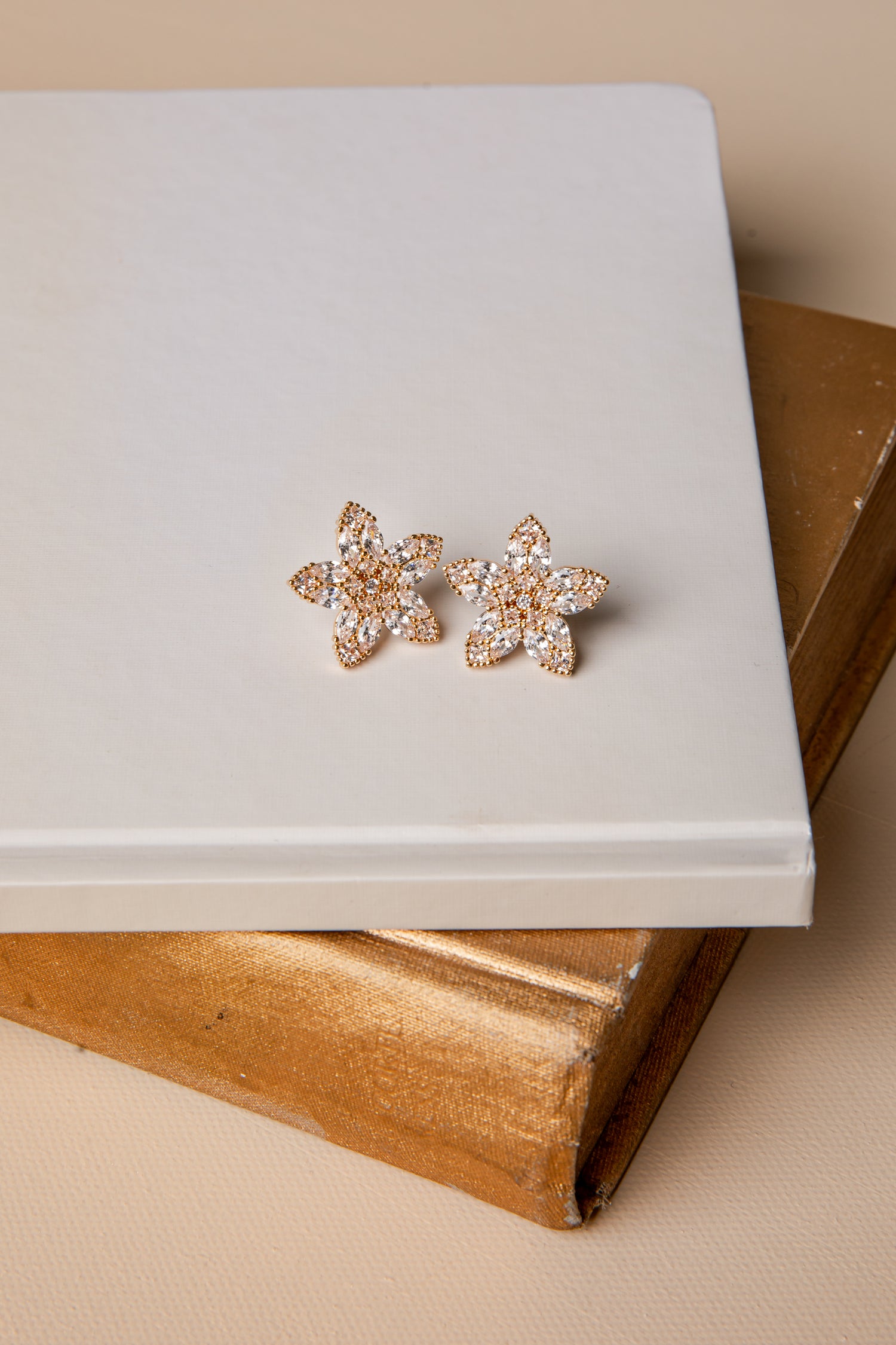 Pair of floral earrings on a white surface with a beige background