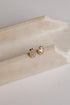 A pair of gold-toned stud earrings with oval clear gemstones and small surrounding clear stones, displayed on a cream-colored stone riser against a light neutral background.