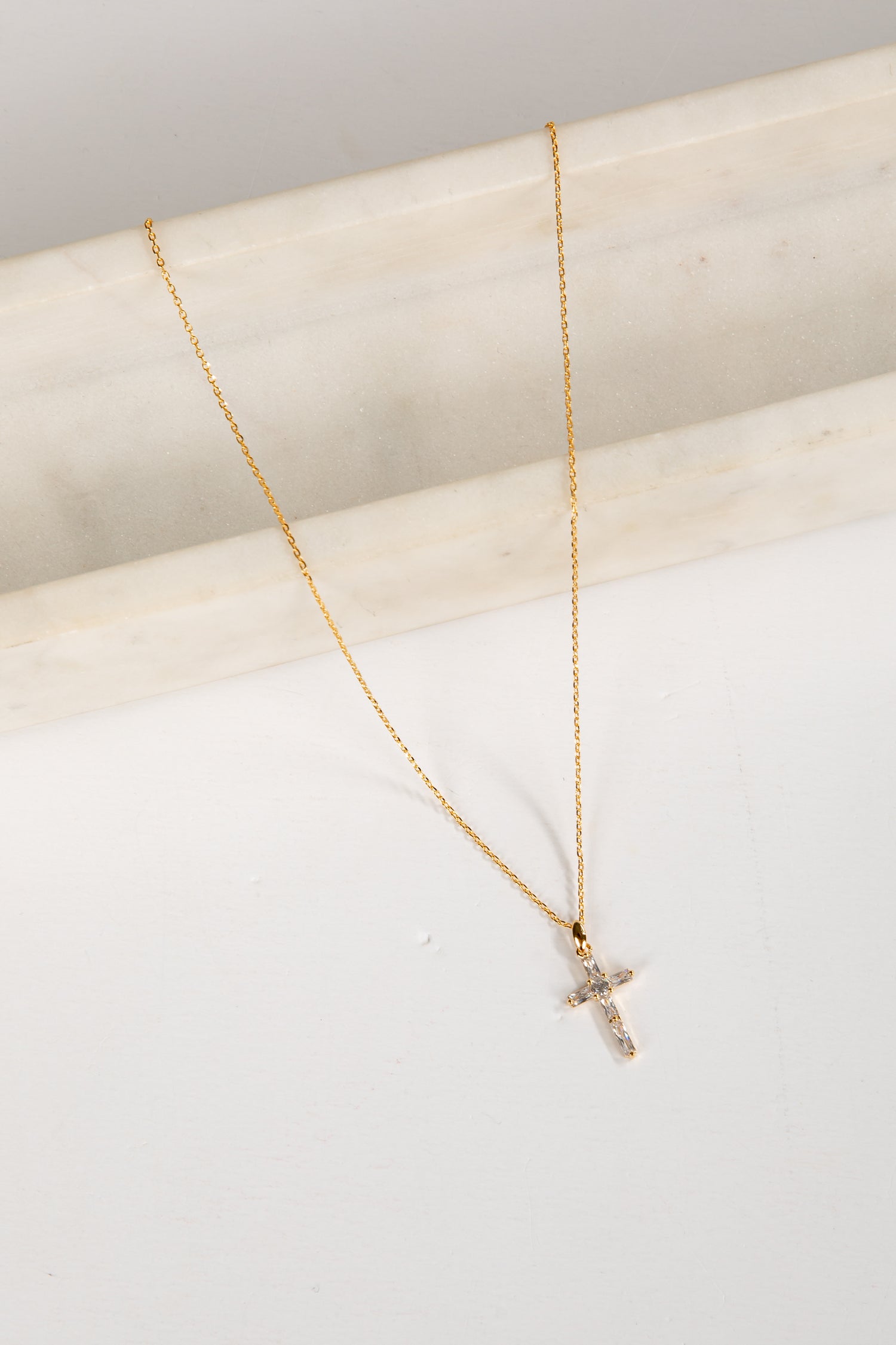 Gold necklace with a small cross pendant on a light background