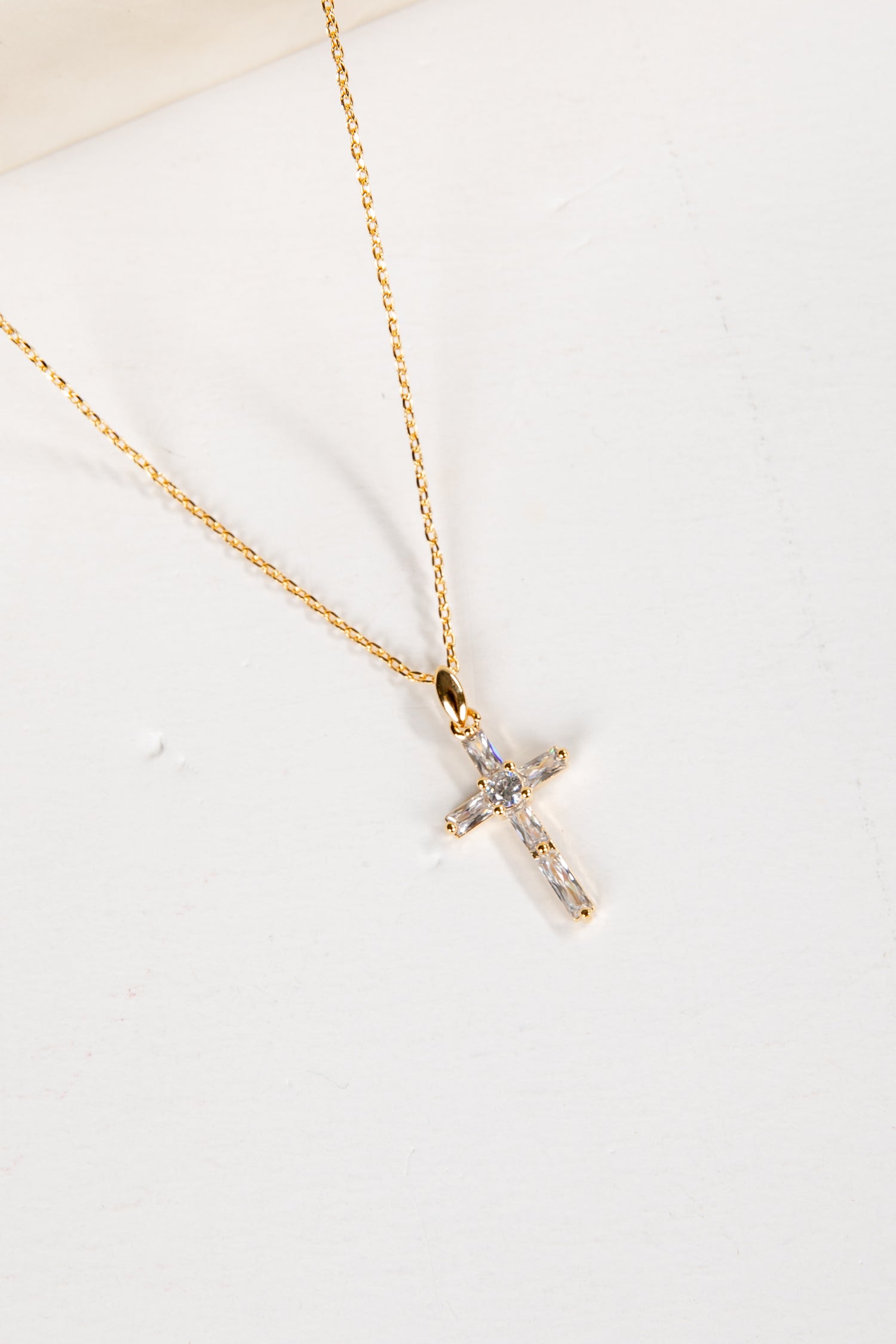 Gold cross necklace with small diamonds on a white background