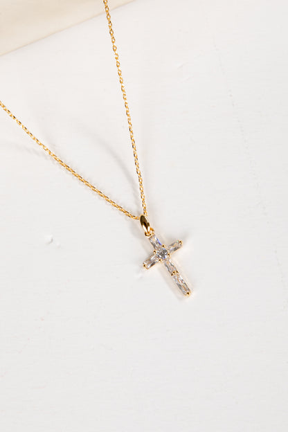 Gold cross necklace with small diamonds on a white background