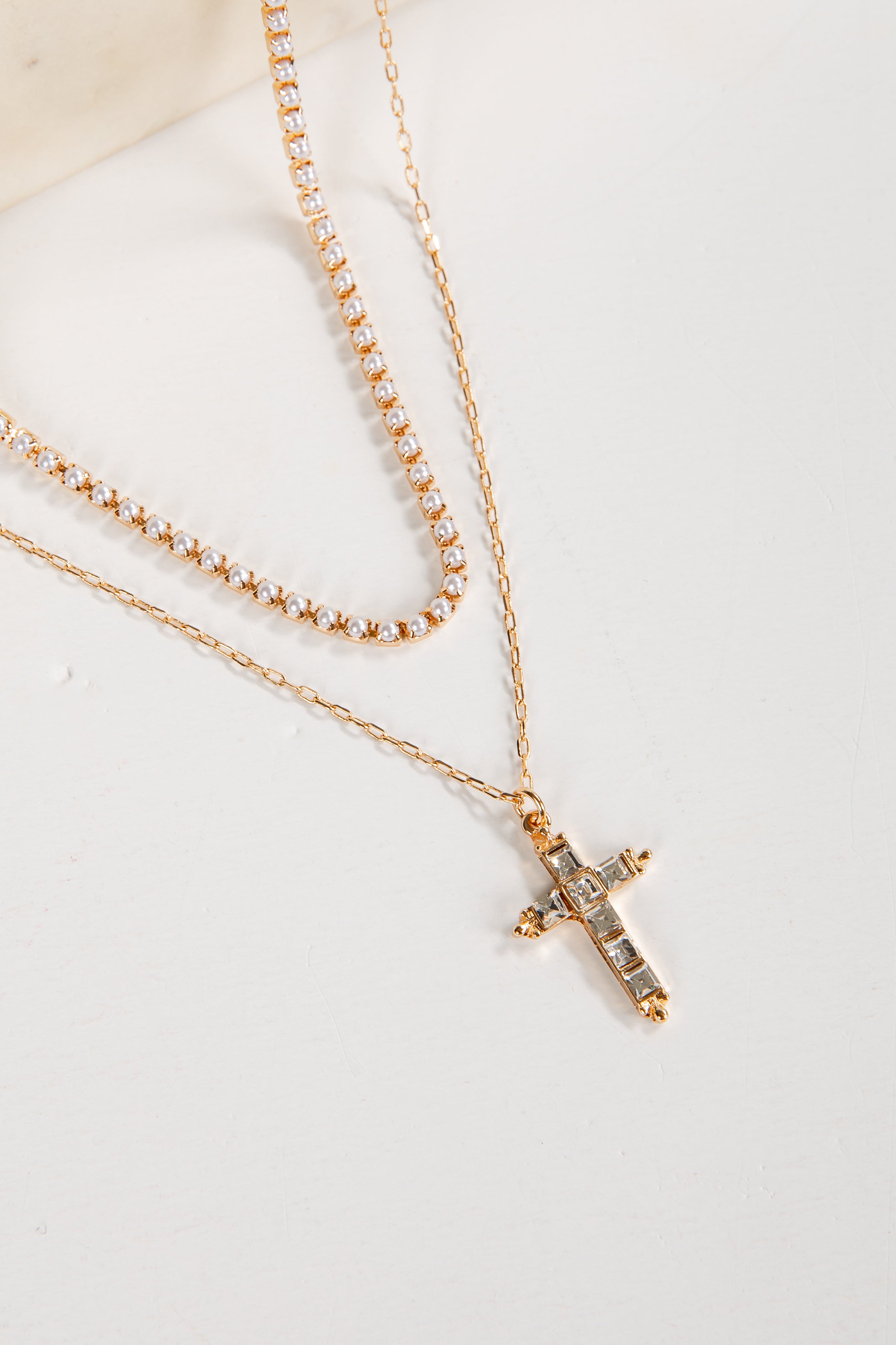 Two gold necklaces with a cross pendant on a light background
