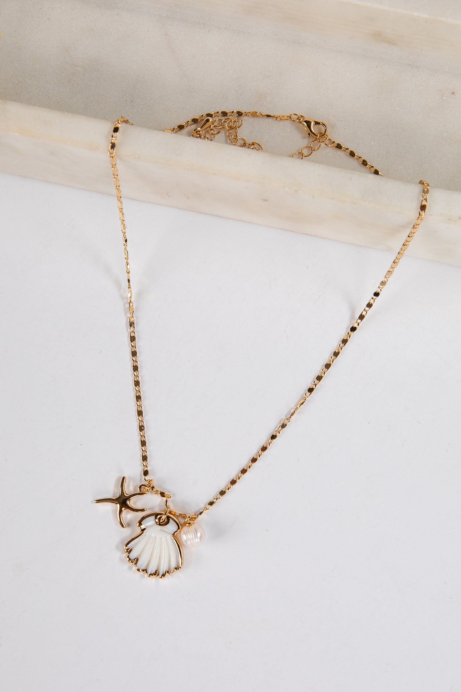Gold necklace with a shell pendant on a light background