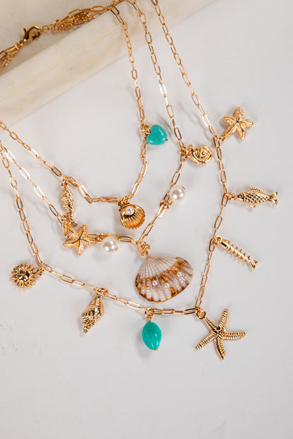 Gold necklaces with various charms including stars, shells, and turquoise beads on a light background.