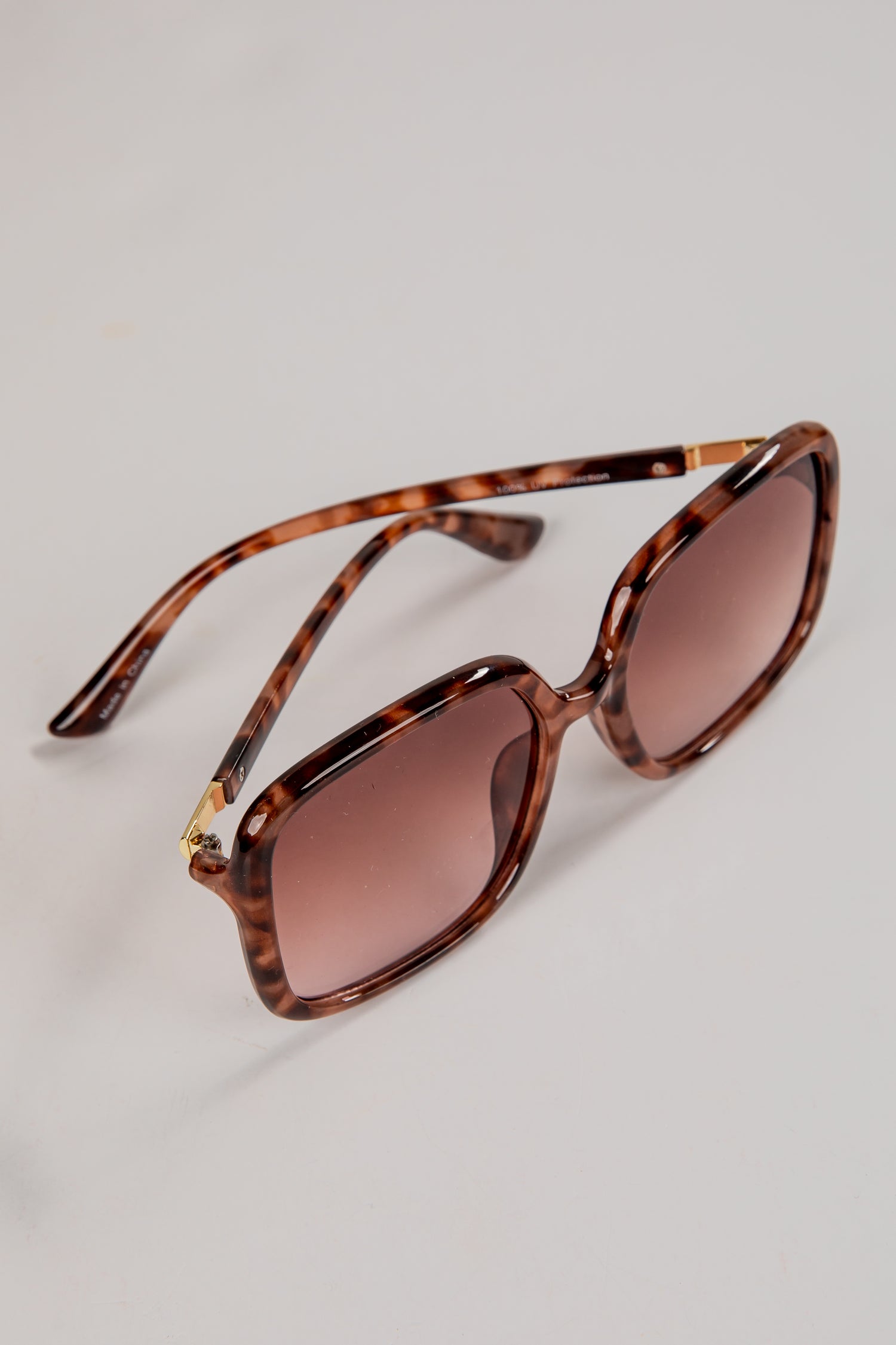 Sunglasses with tortoiseshell frame and brown lenses on a light gray background