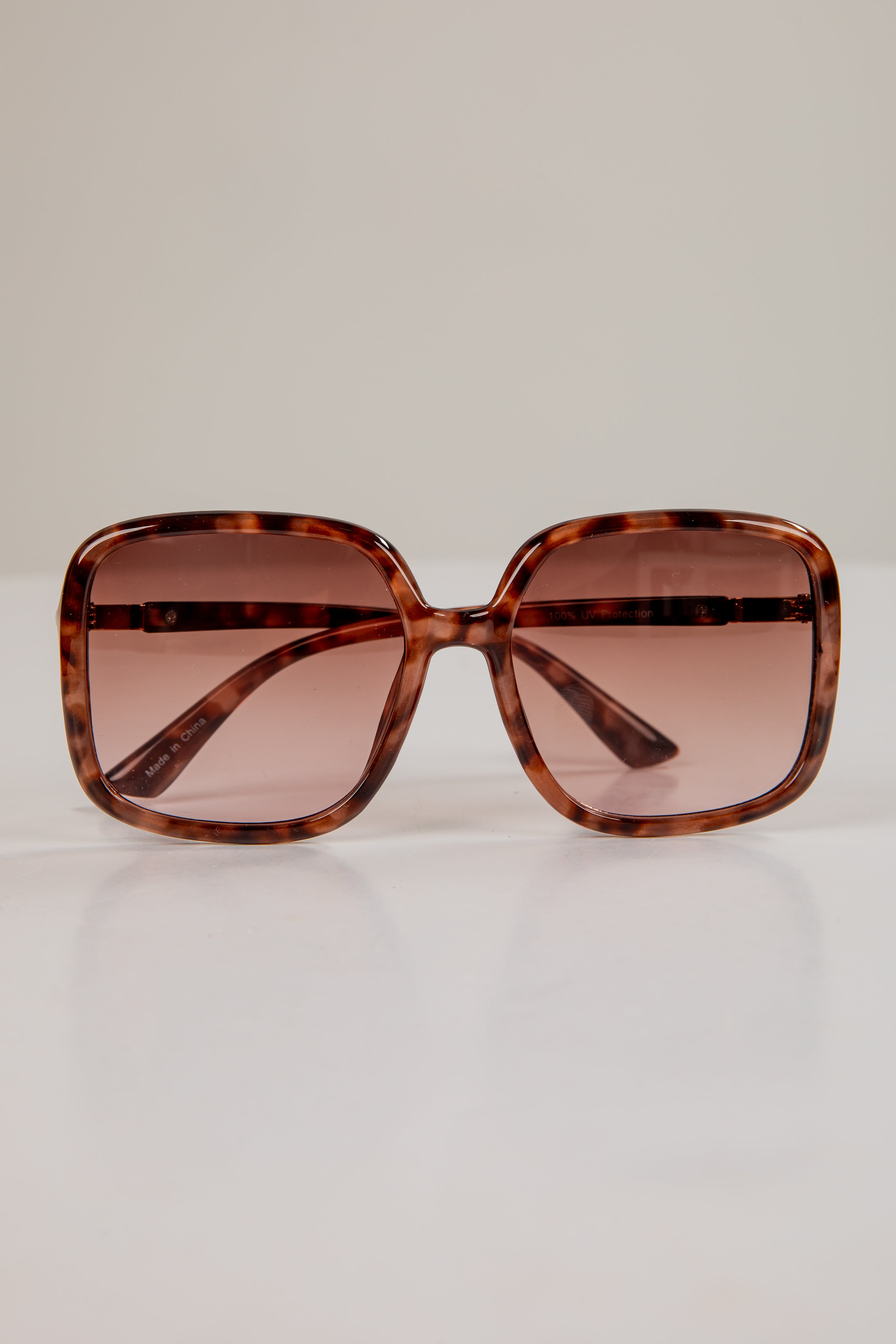 Sunglasses with tortoiseshell frame and brown lenses on a light beige background