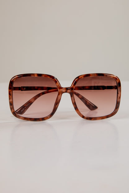 Sunglasses with tortoiseshell frame and brown lenses on a light beige background