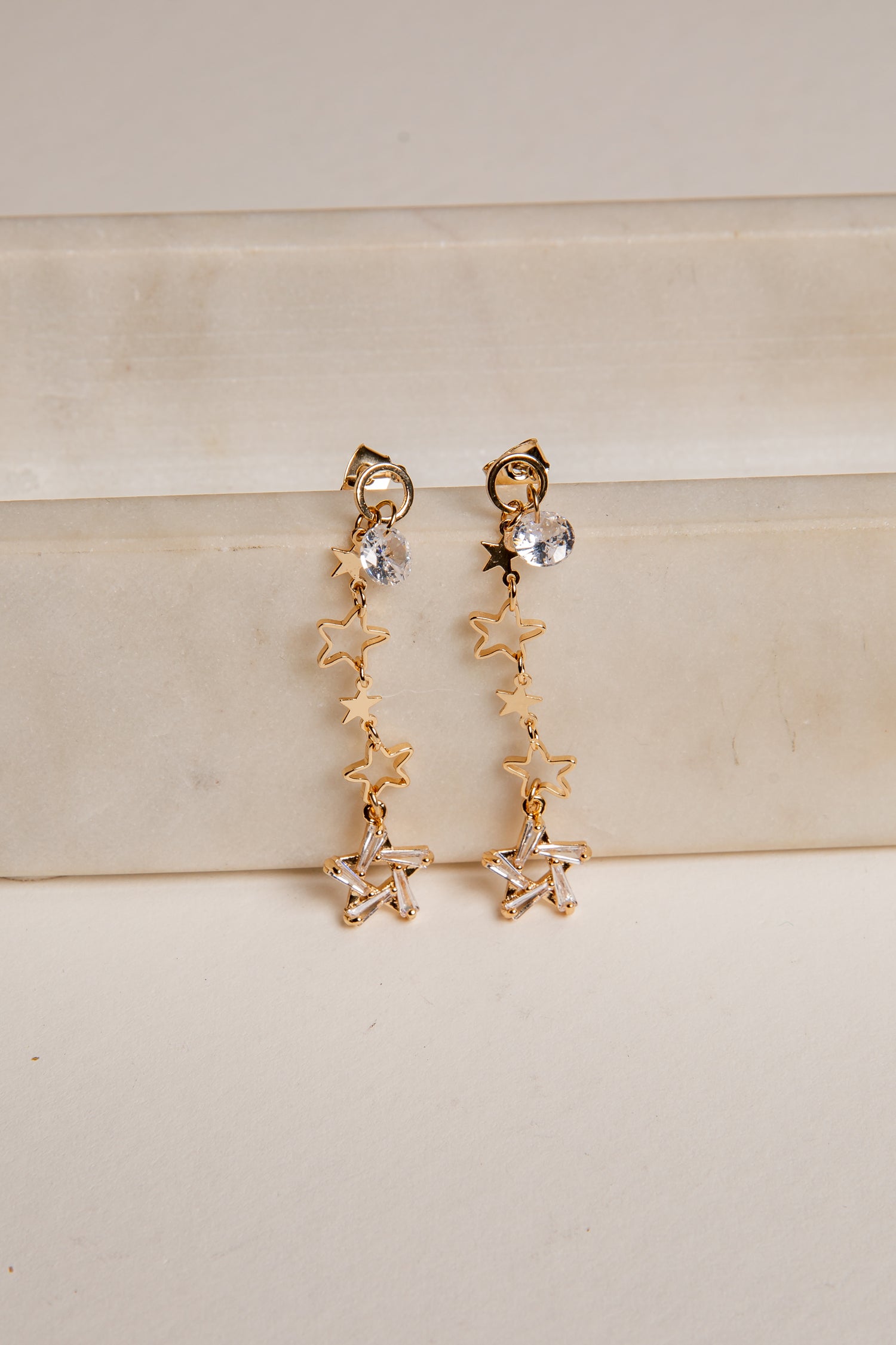 Gold star-shaped earrings on a beige surface
