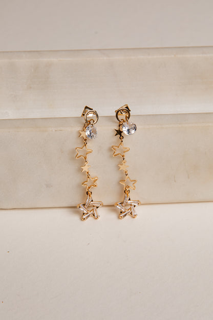 Gold star-shaped earrings on a beige surface