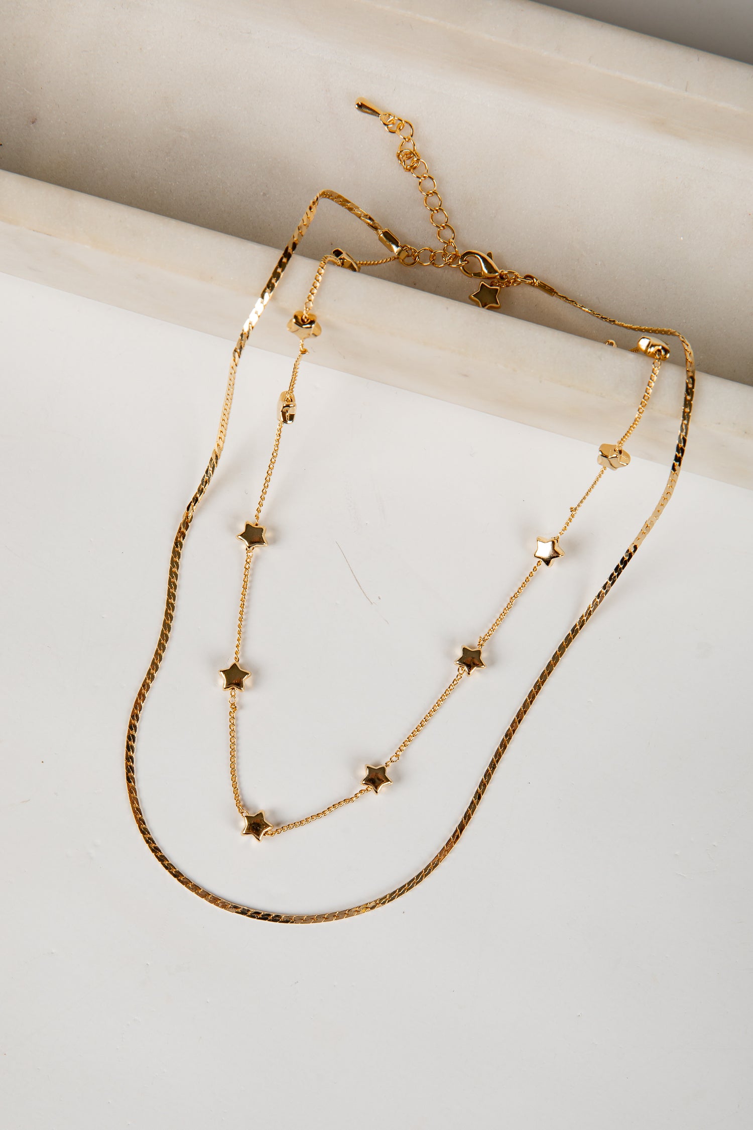 Gold necklace with star-shaped beads on a marble surface