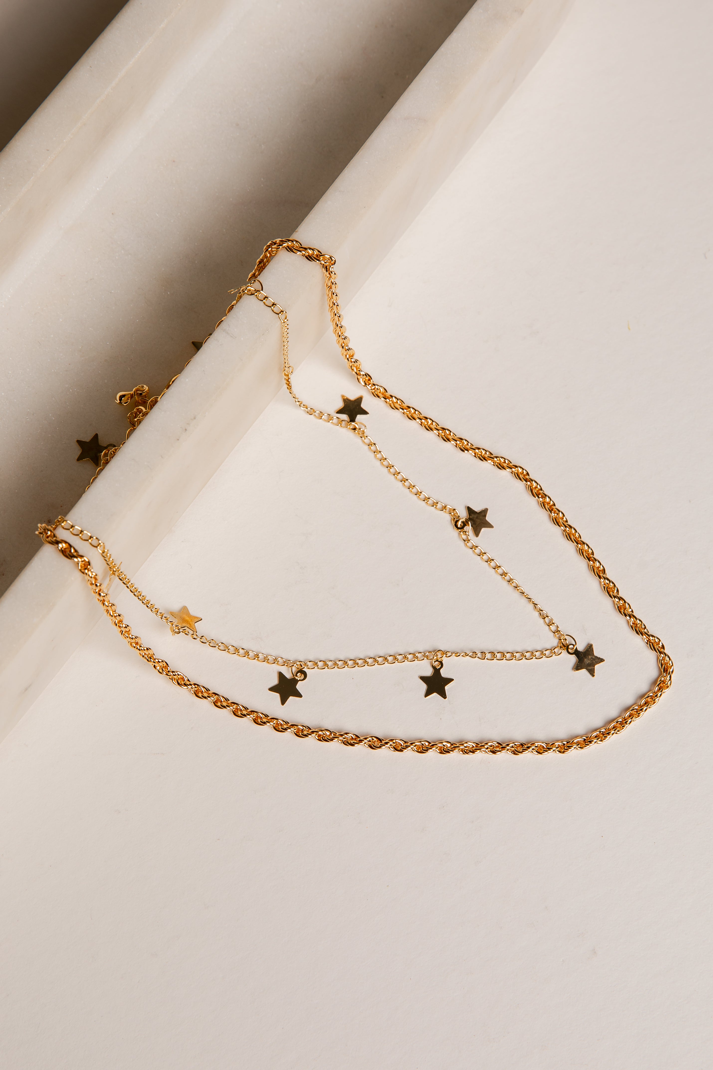 Gold chain necklace with star pendants on a white surface
