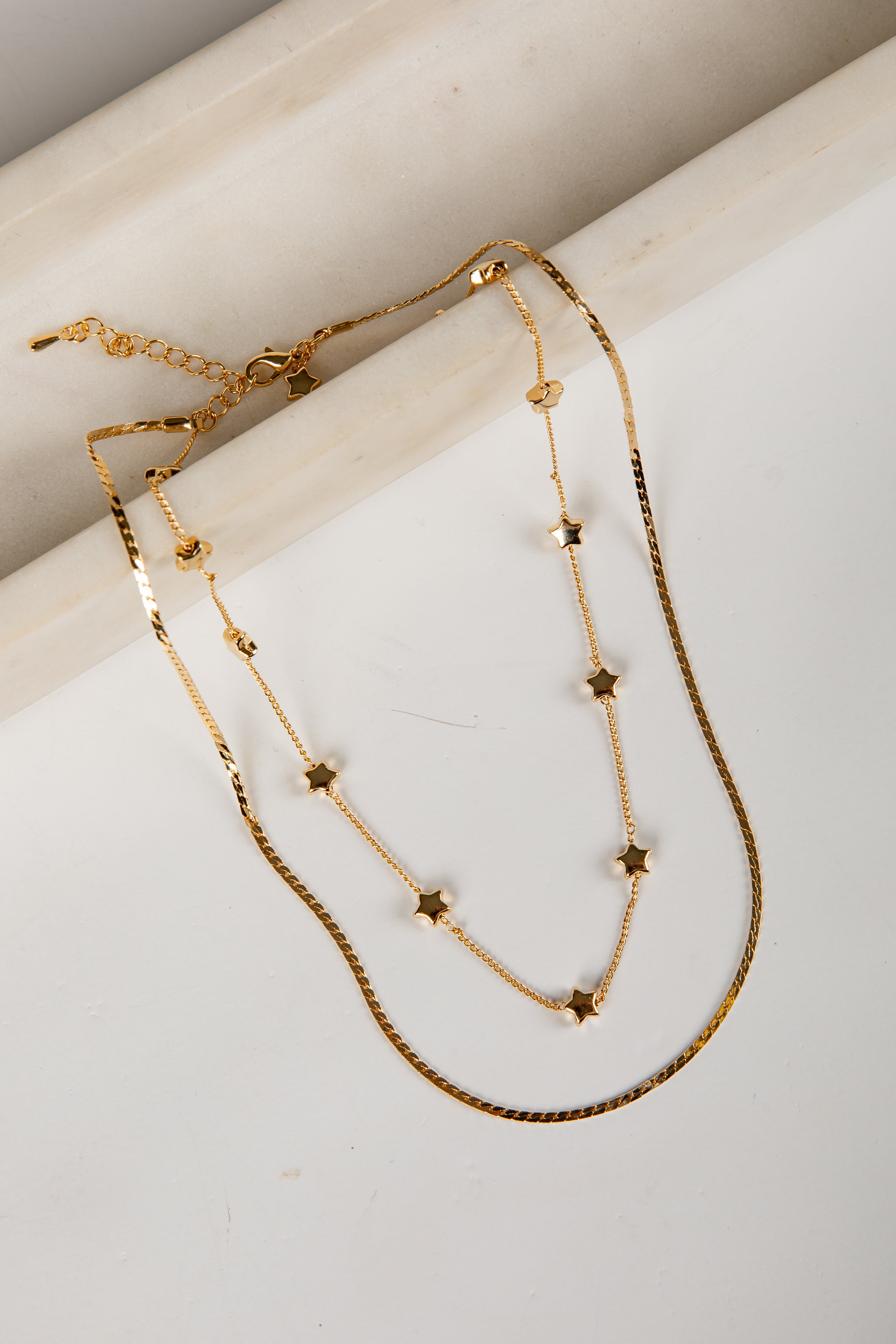 Two gold necklaces with star-shaped beads on a light background