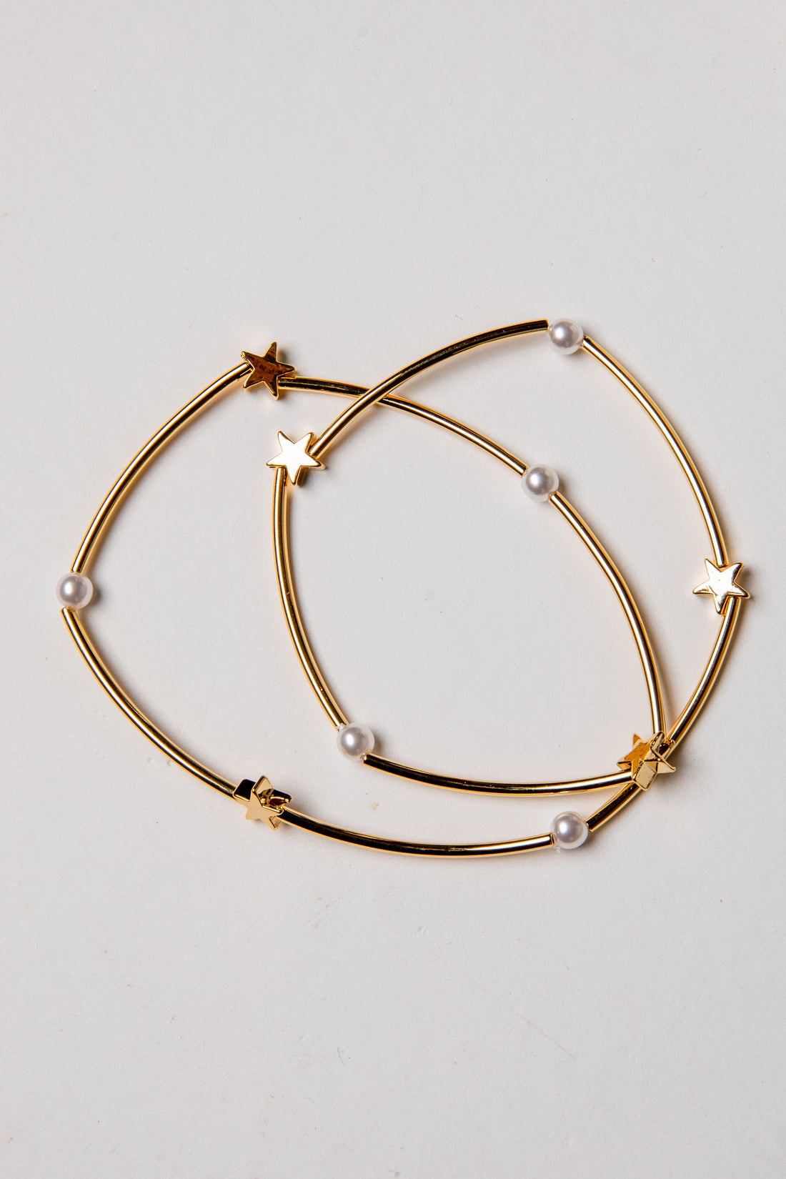 Gold hoop earrings with star and pearl accents on a light gray background