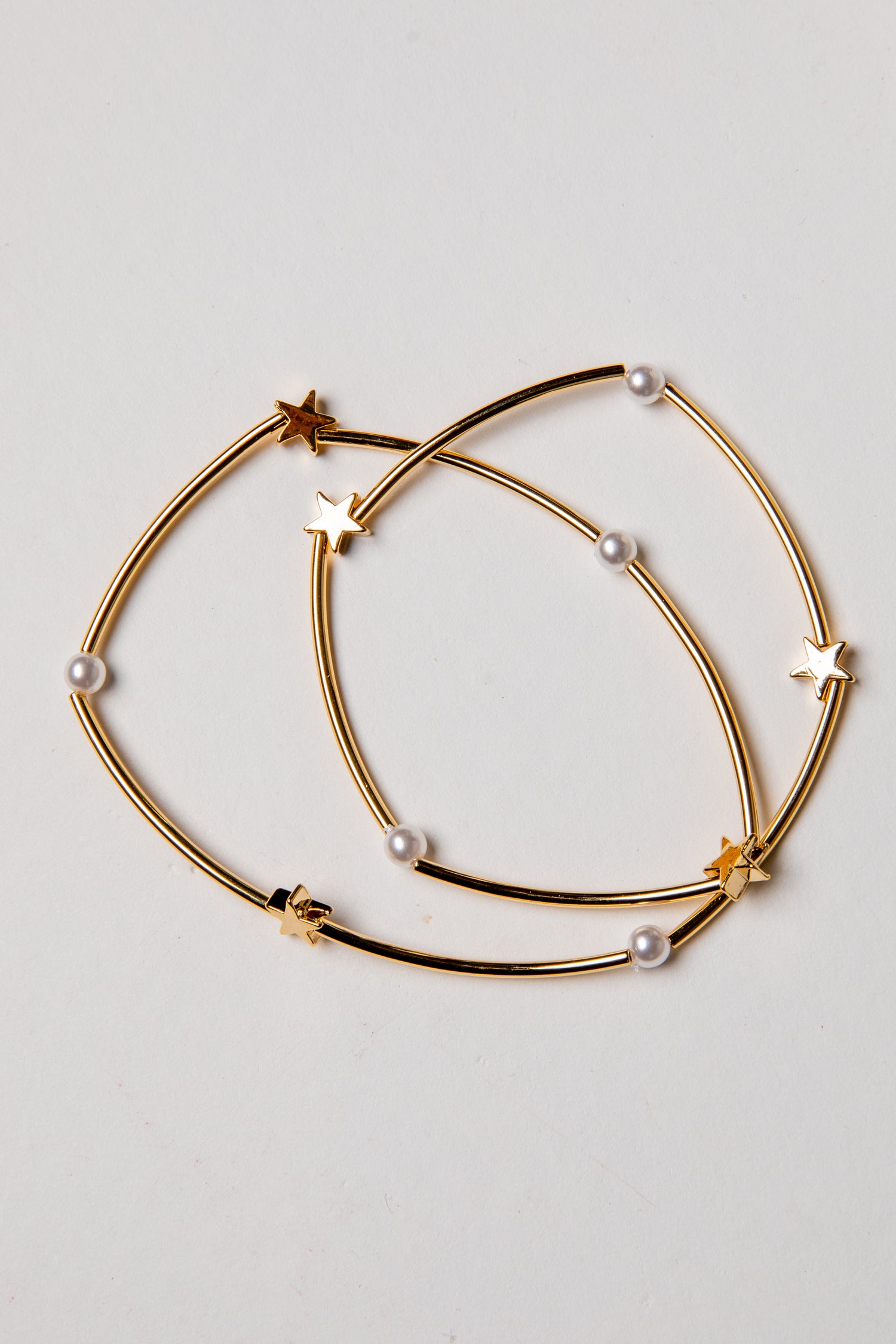 Gold hoop earrings with star and pearl accents on a light gray background