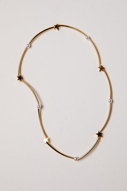 Gold necklace with star and pearl accents on a light gray background