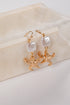 Gold starfish earrings with pearl-like beads on a beige stone surface