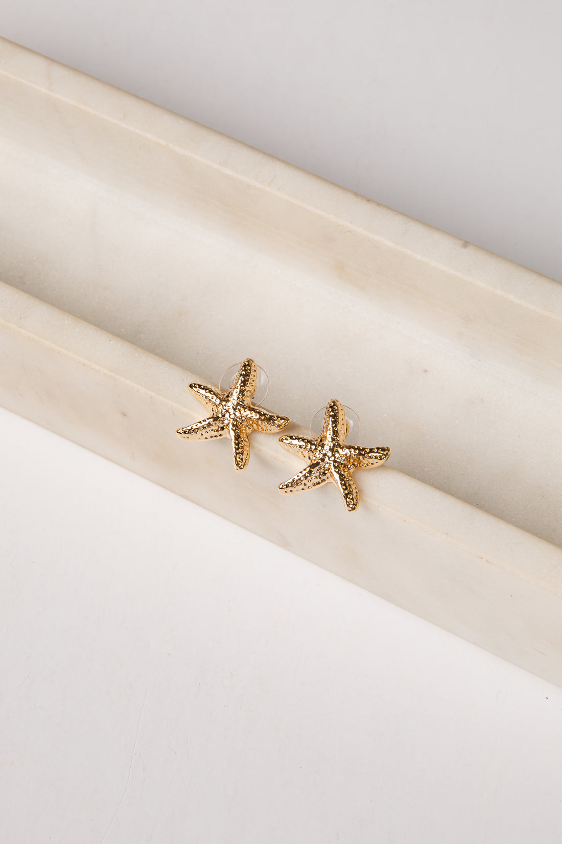Gold starfish earrings on a white surface