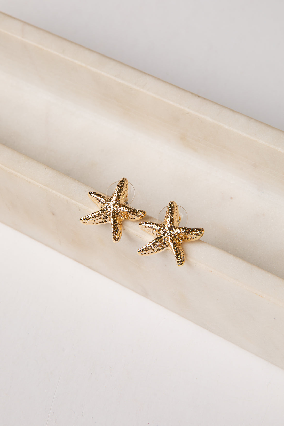 Gold starfish earrings on a white surface