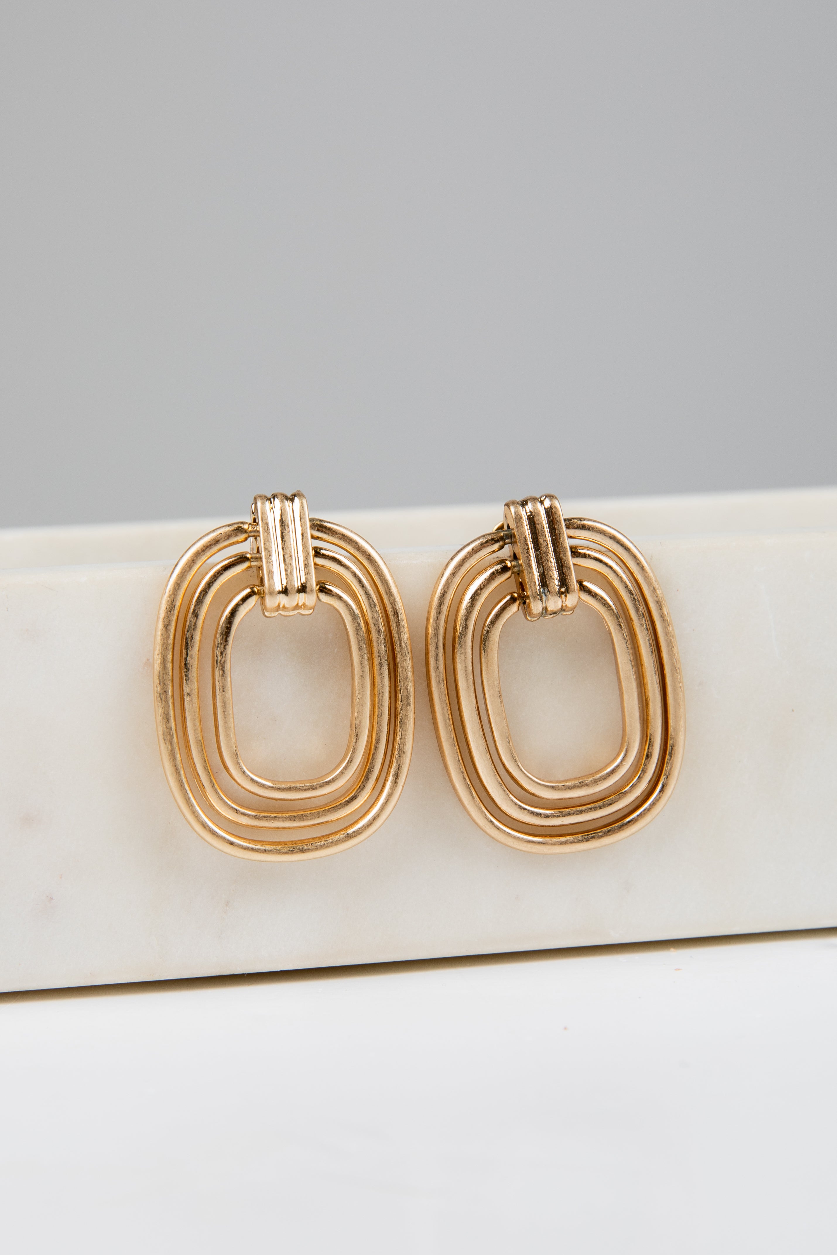 Gold hoop earrings on a white surface with a gray background
