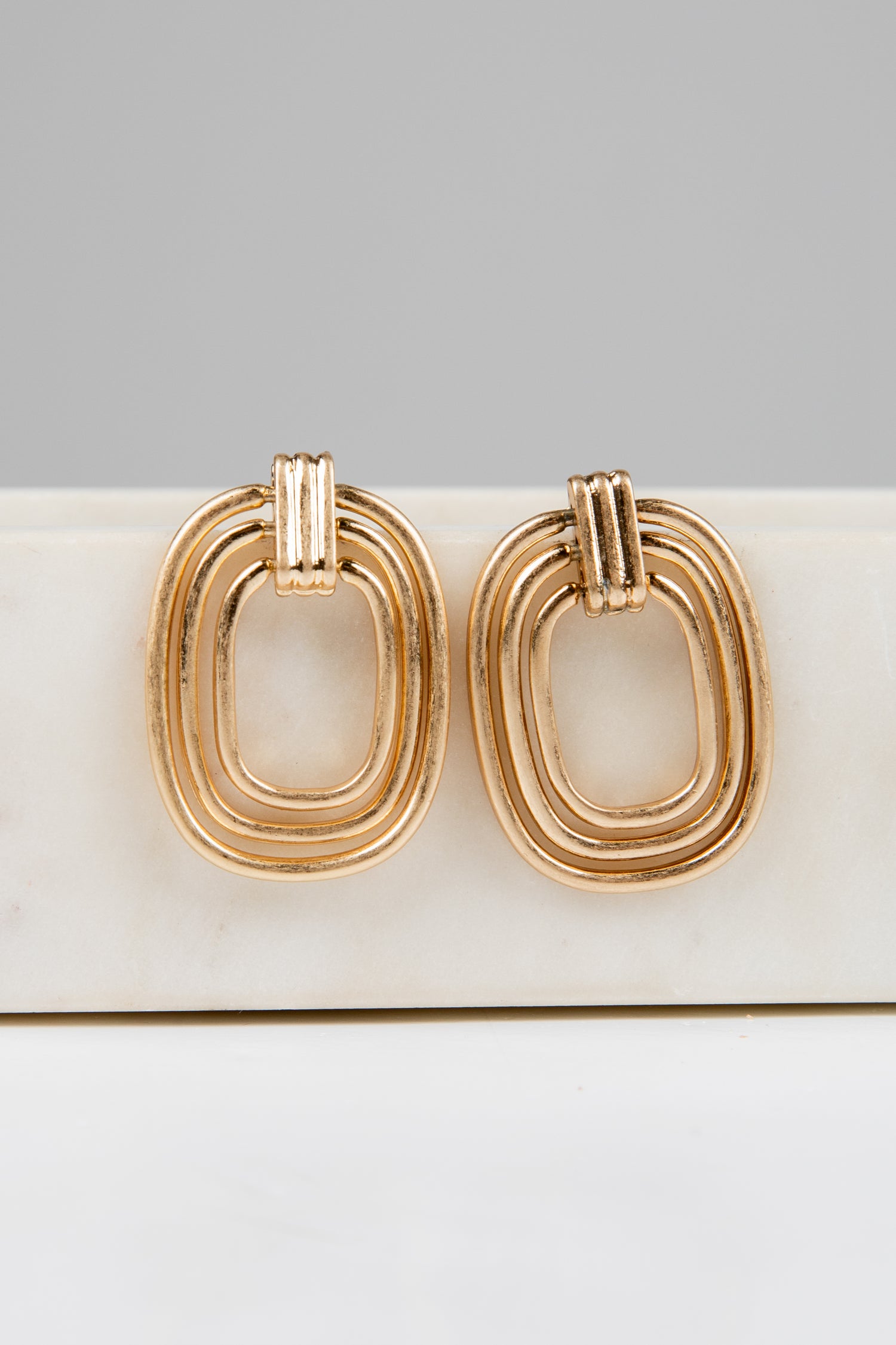Gold hoop earrings on a white surface with a gray background
