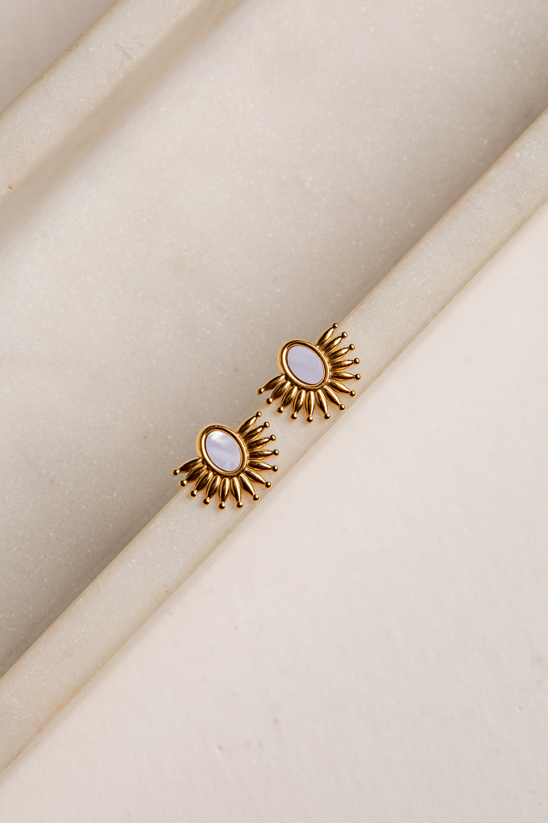 Gold earrings with a central gemstone on a beige fabric background