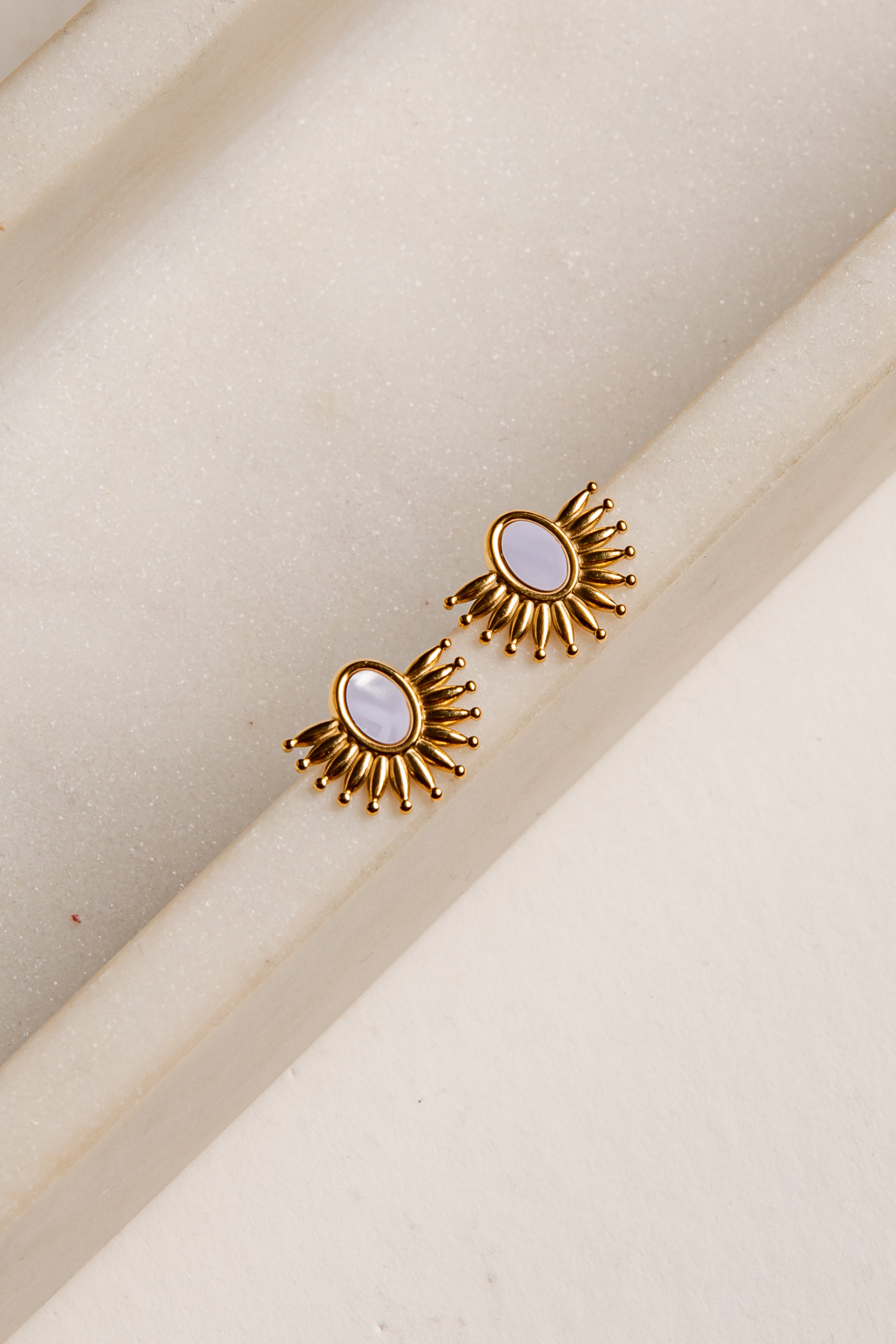 Gold earrings with a central gemstone on a beige background