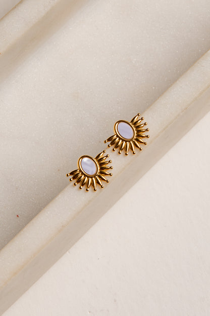 Gold earrings with a central gemstone on a beige background