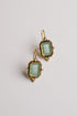 A pair of antique-style gold drop earrings featuring light green carved glass panels with classical figures, accented with small white pearls, shown on a plain light background.
