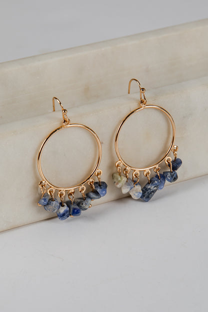Gold hoop earrings with blue gemstones on a light background