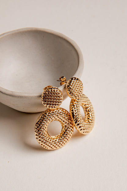 Gold hoop earrings on a light beige surface with a ceramic bowl in the background