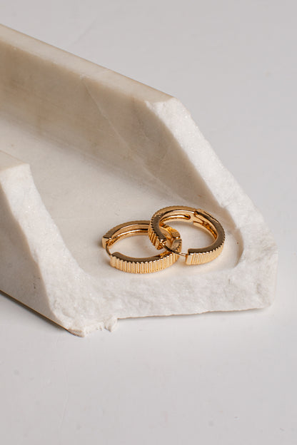 Two gold textured hoop earrings resting on a white stone tray against a light gray background.