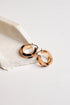 A pair of polished rose gold hoop earrings resting on a textured white stone slab against a clean white background.