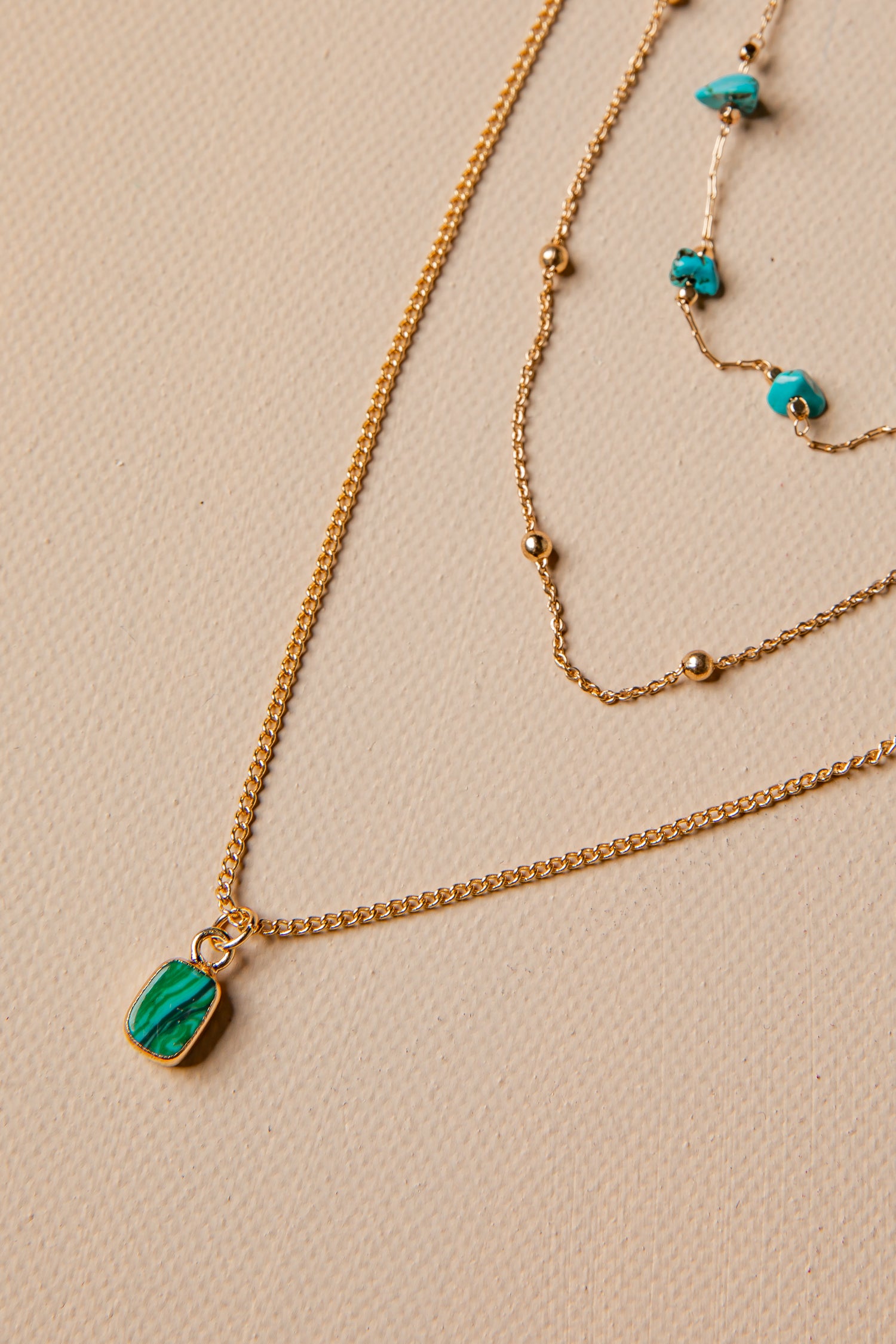 Two gold necklaces with green gemstones on a beige background