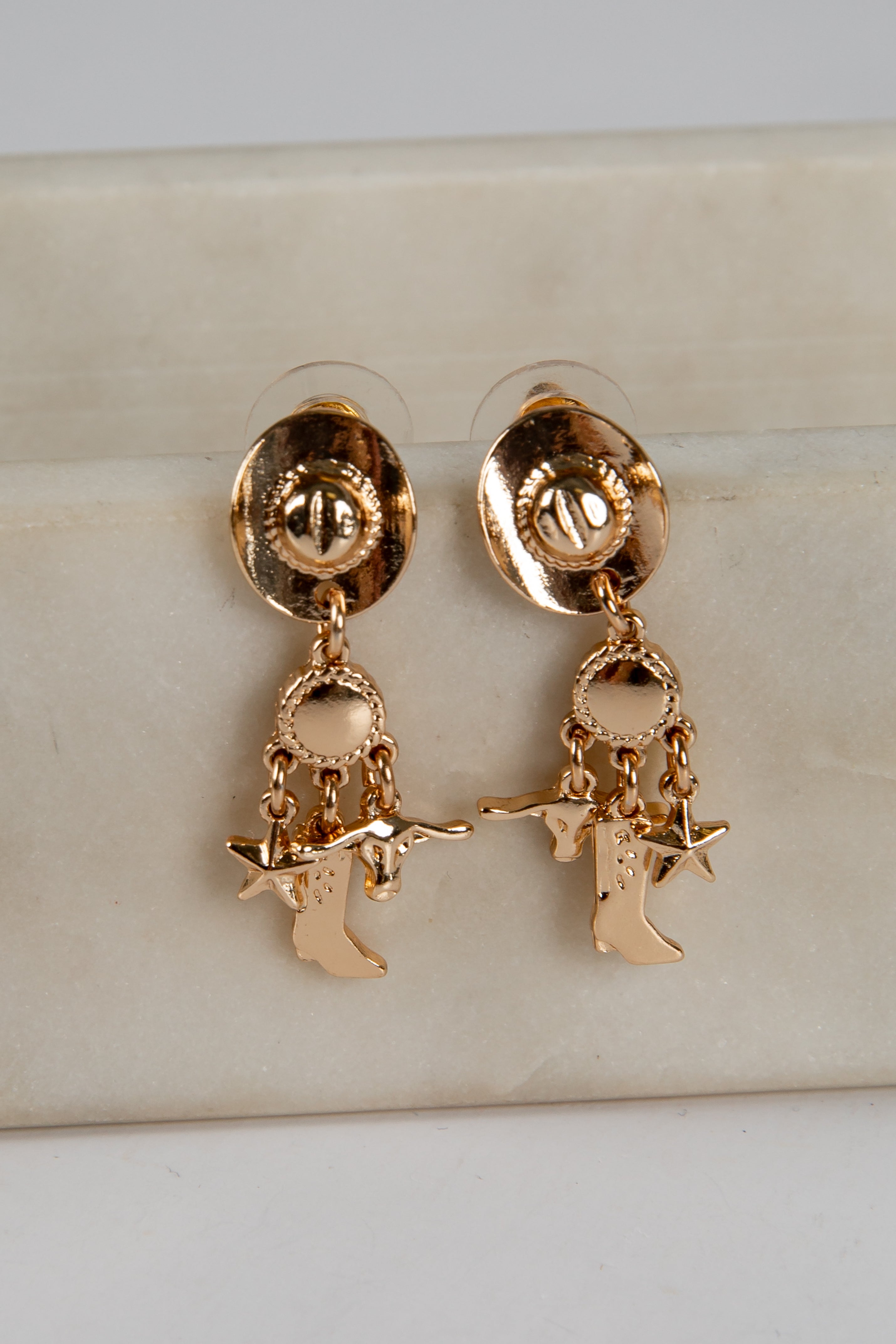 Gold earrings with star and figure charms on a beige surface
