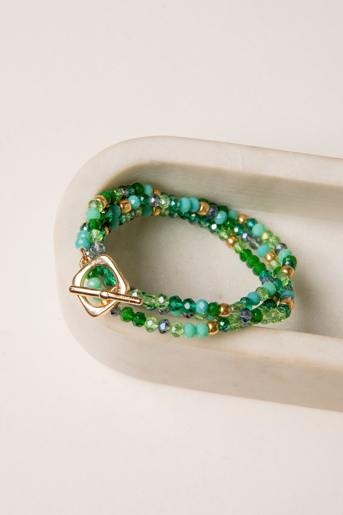 Green beaded bracelet with gold accents on a beige surface