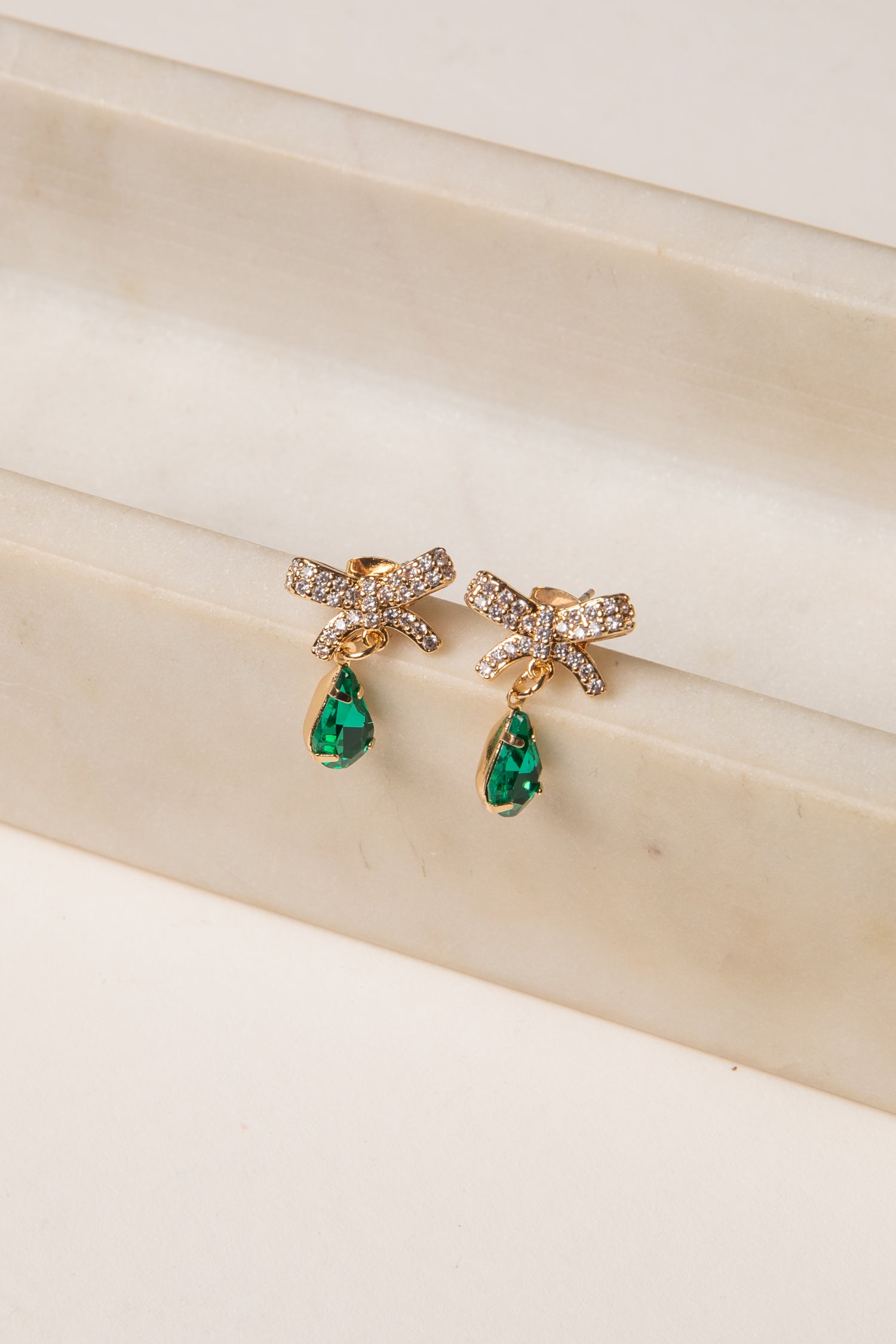 Gold earrings with green gemstones on a beige surface