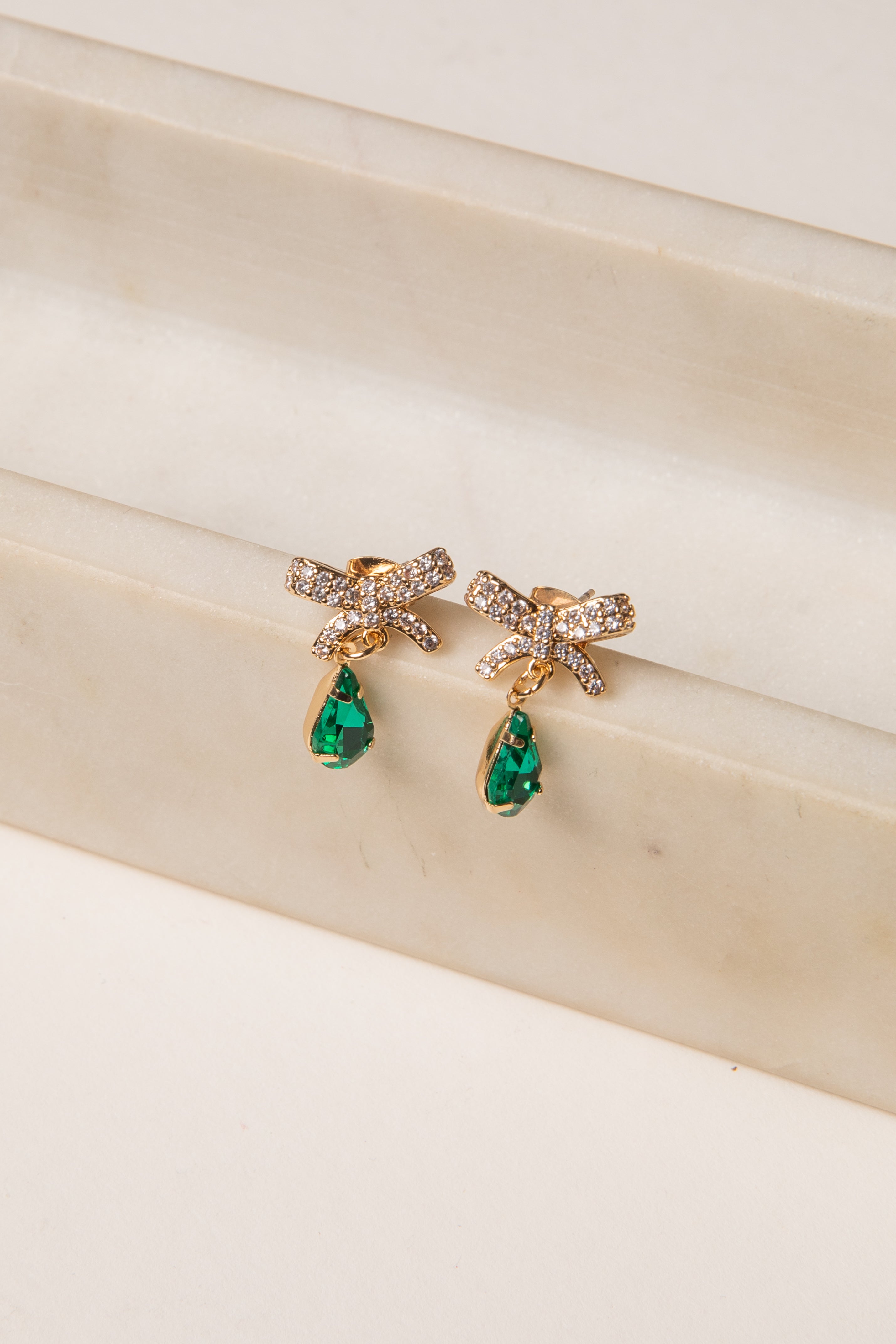 Gold earrings with green gemstones on a beige surface