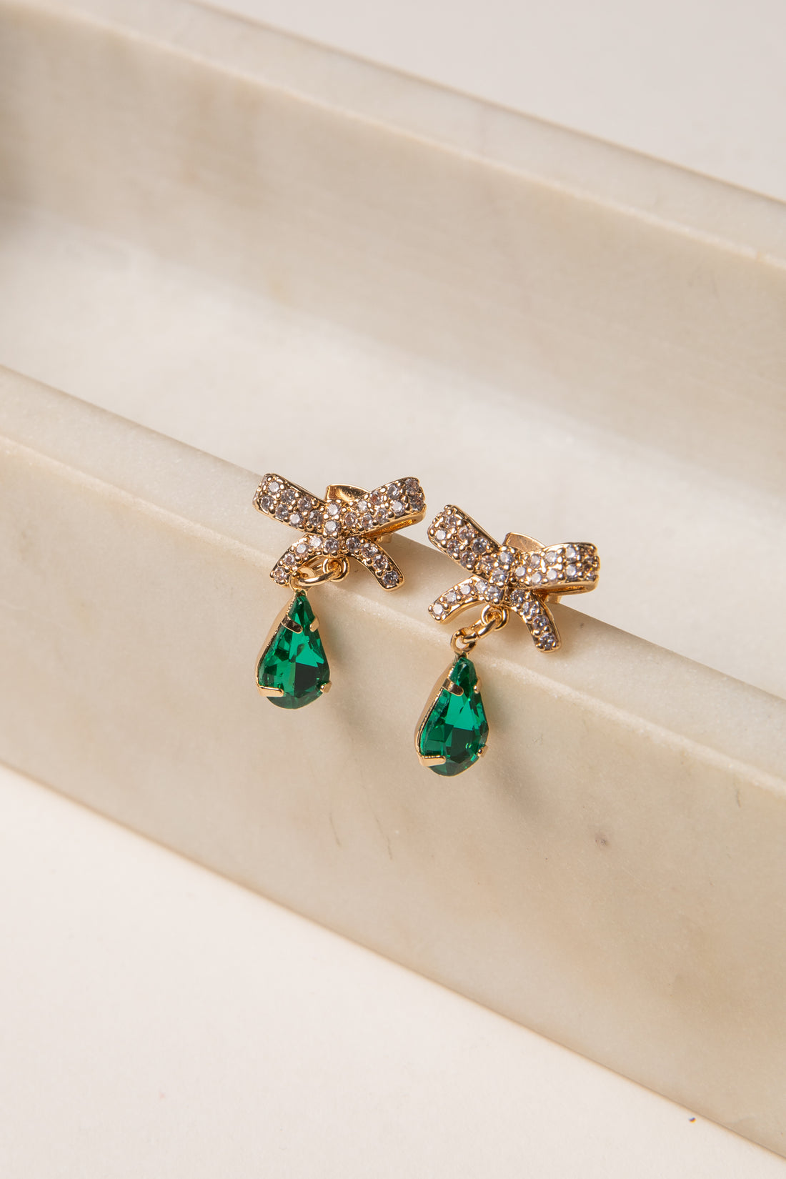 Gold earrings with green gemstones on a beige surface