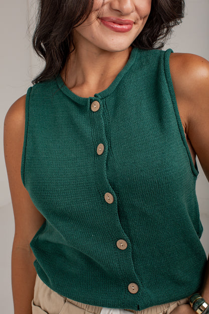 A close-up of a woman wearing a sleeveless, ribbed knit top in forest green with a button-down front. The top features light brown wooden buttons.