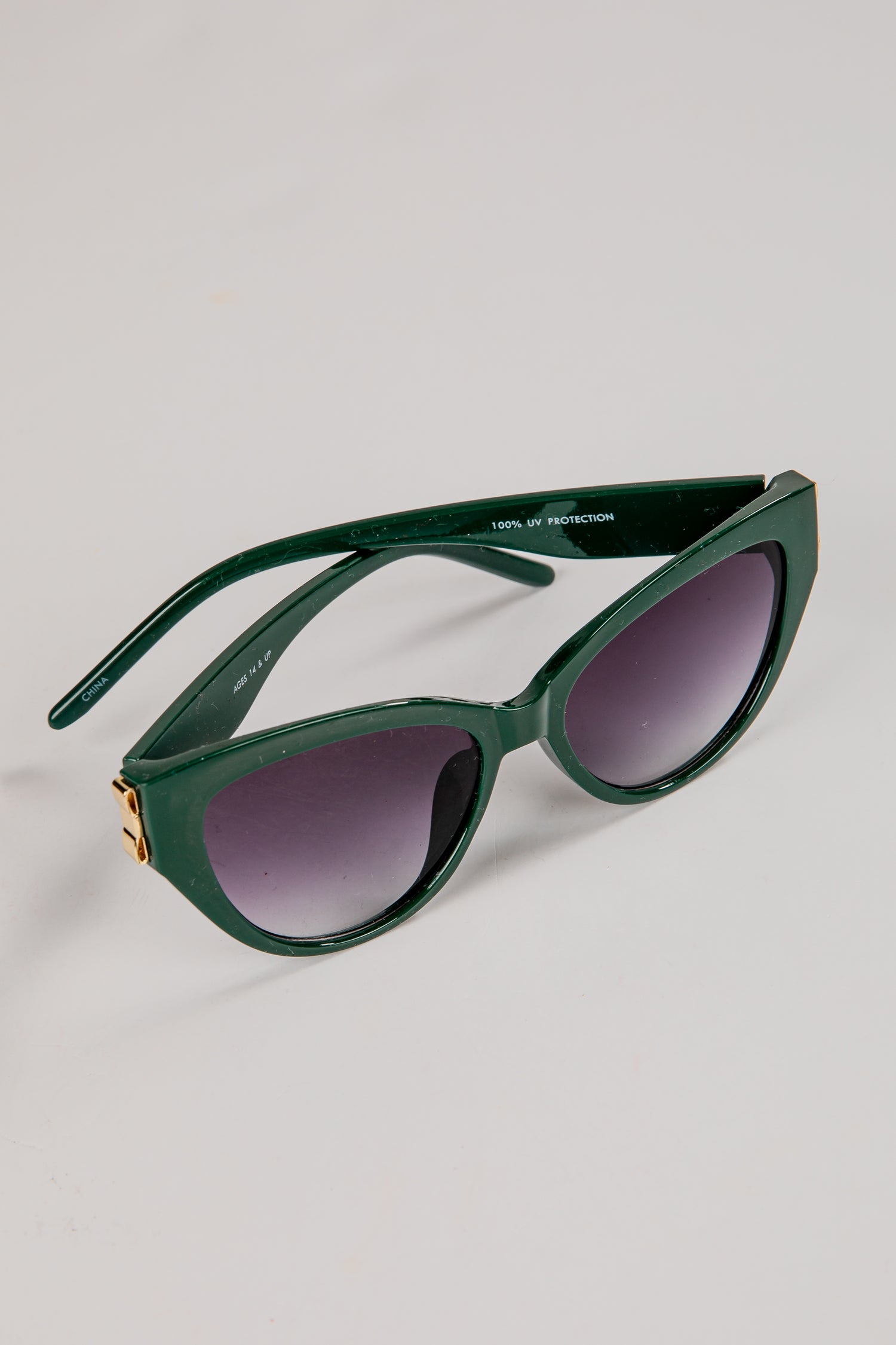 Green sunglasses with dark lenses on a light gray background