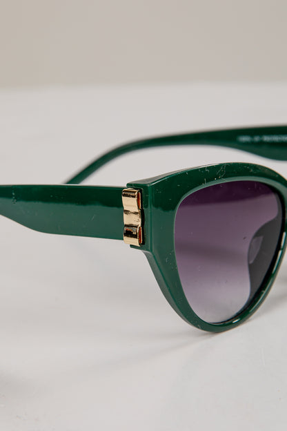 Green sunglasses with a gold accent on a light gray background