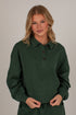 A woman modeling a dark forest green long-sleeve polo shirt with a buttoned collar, set against a plain light gray studio background.