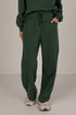 A person wearing dark green drawstring sweatpants with a matching sweatshirt, standing against a plain light gray studio background.