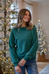 Woman wearing a teal sweater standing in front of Christmas trees.