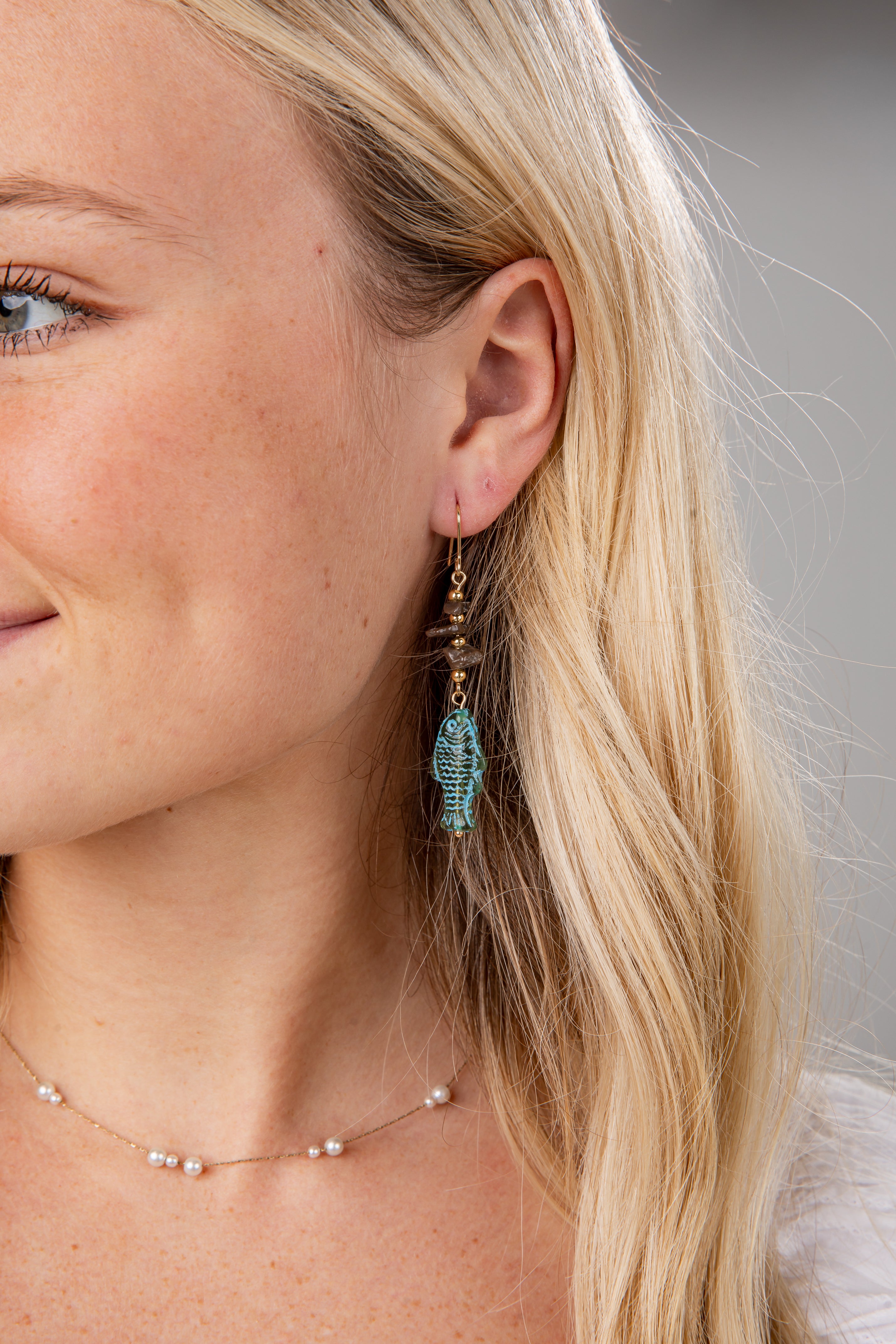 Close-up of a woman wearing turquoise earrings with a neutral background