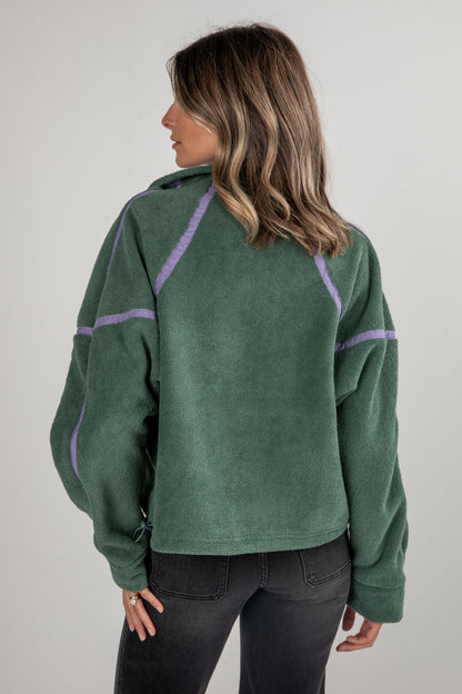 Person wearing a green fleece pullover with purple accents on a plain background