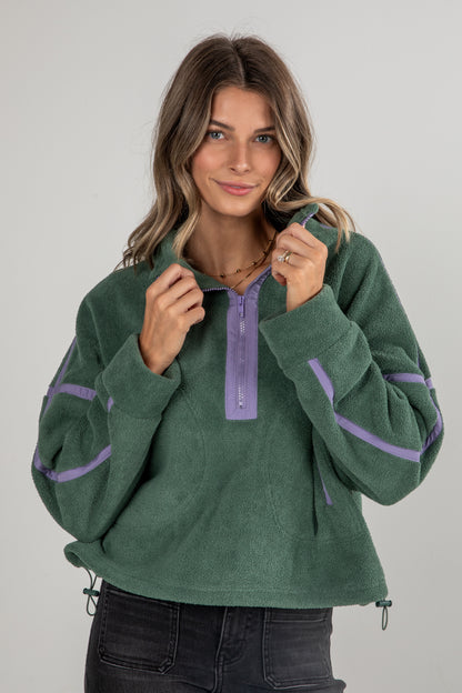 Woman wearing a green fleece pullover with purple accents on a gray background