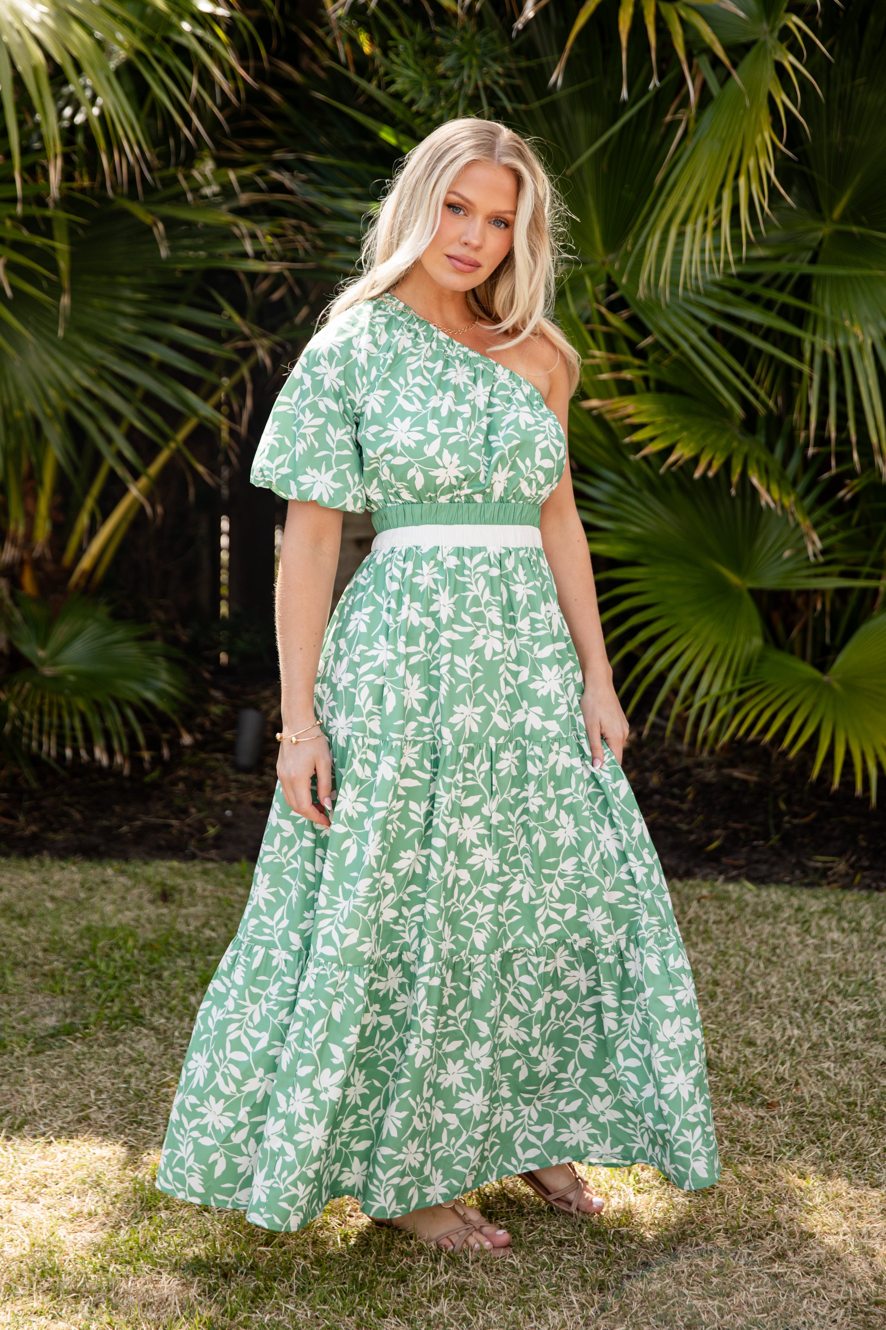 Woman wearing a green floral dress standing in front of palm trees