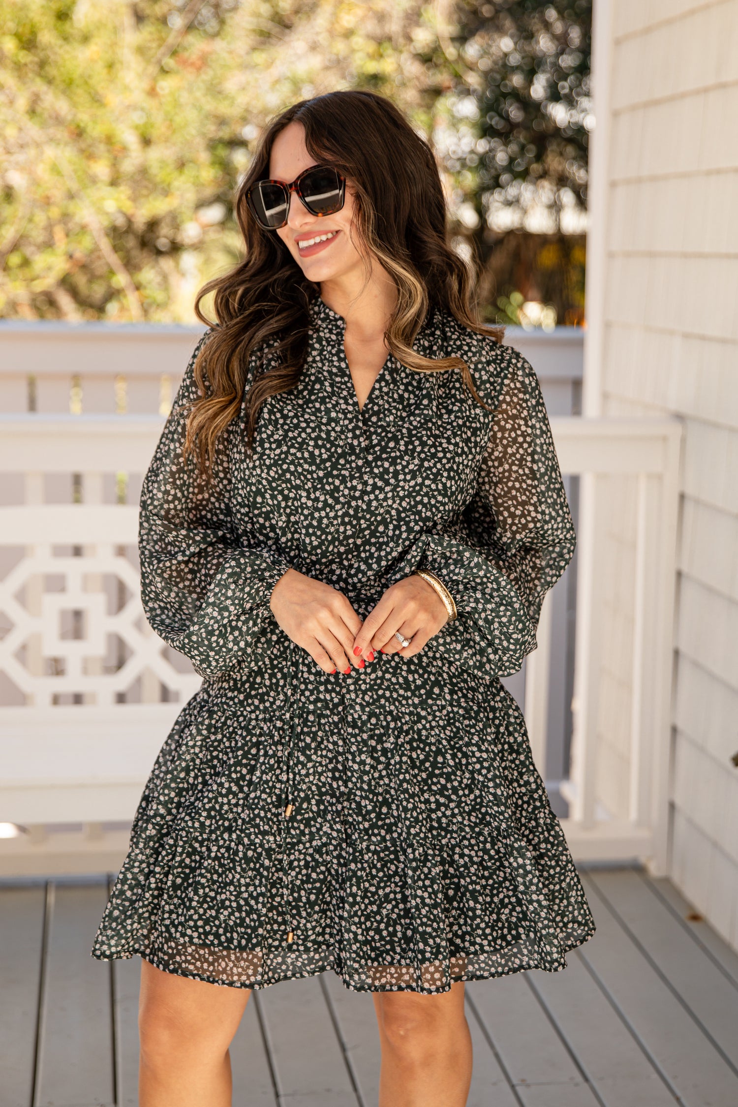 Woman wearing a black floral dress on a wooden deck with trees in the background