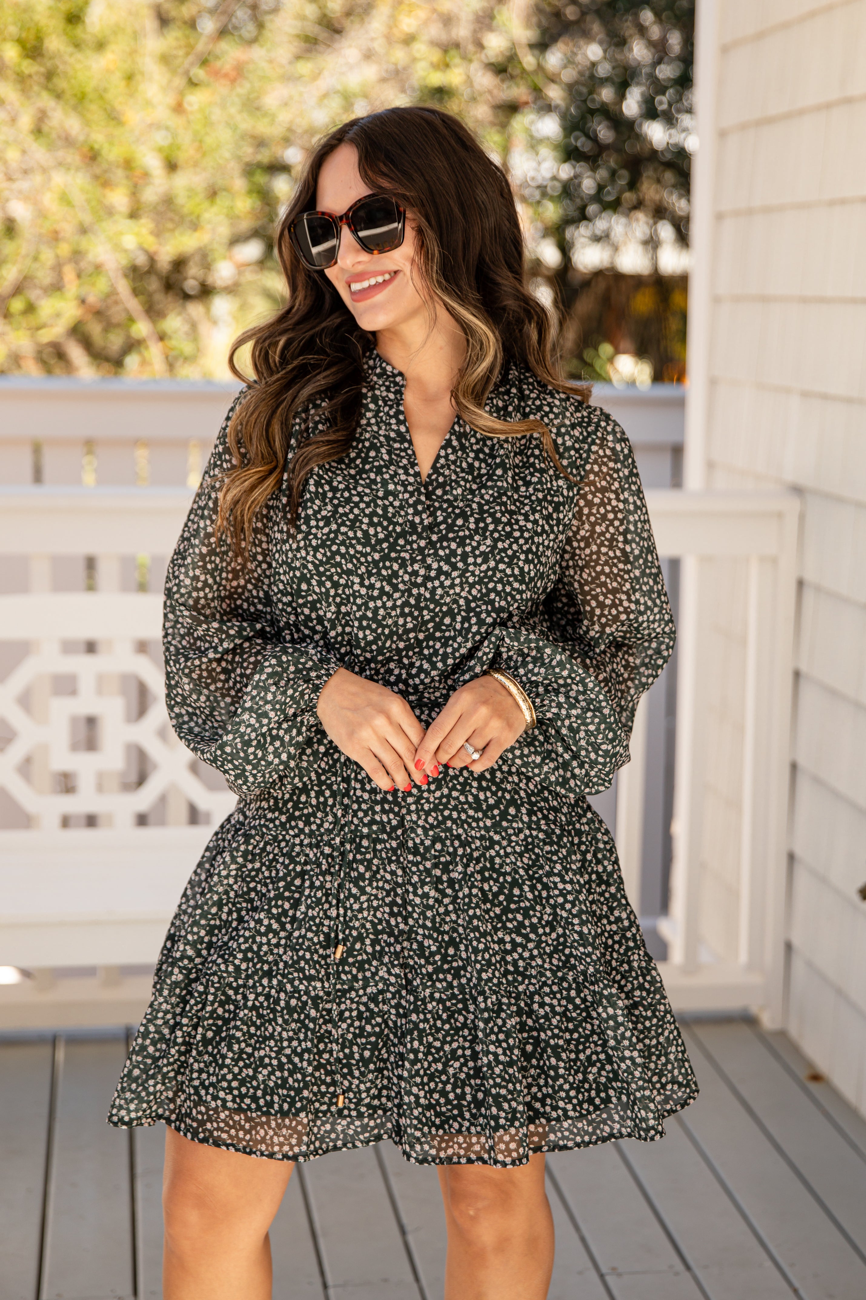 Woman wearing a black floral dress on a wooden deck with trees in the background